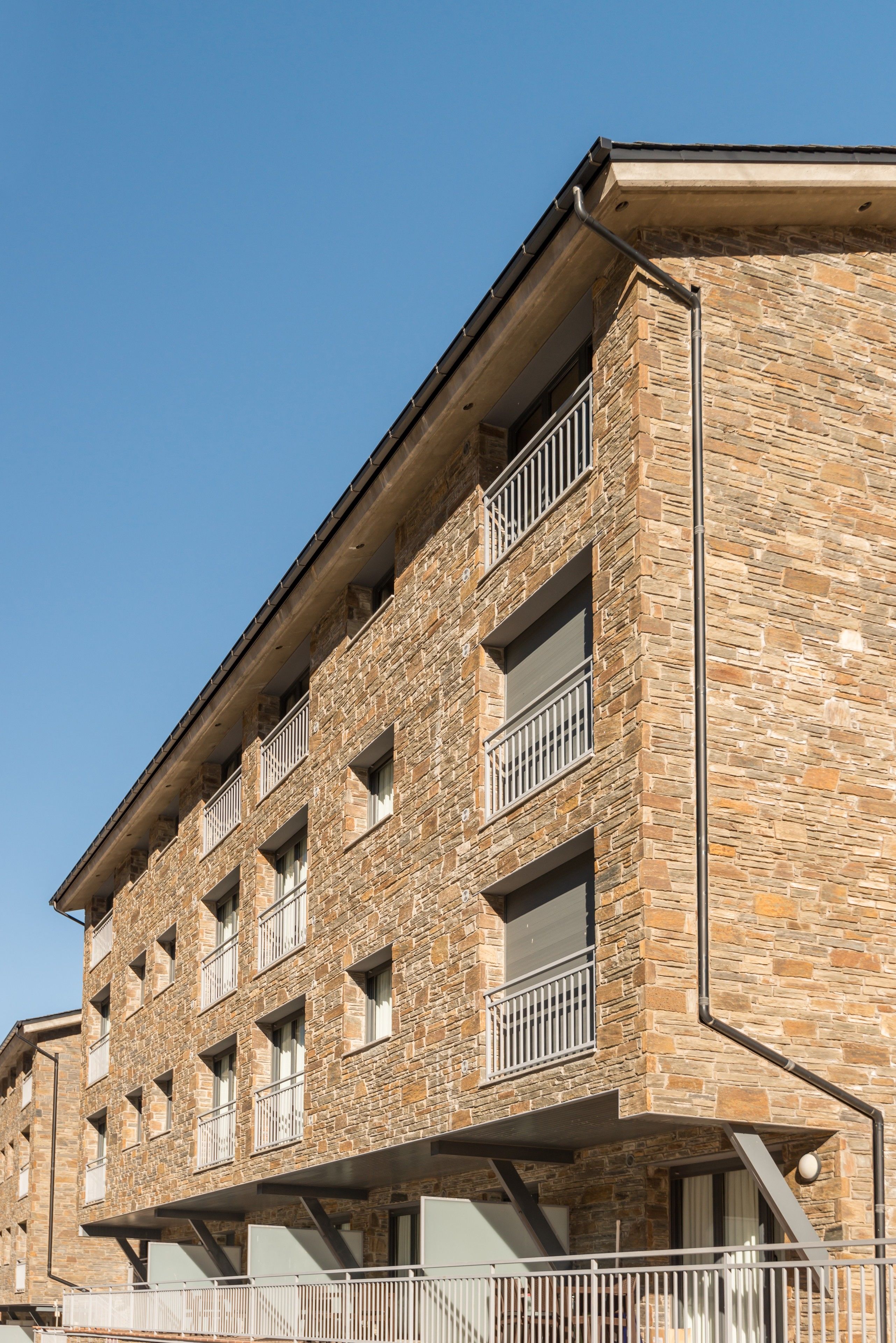 A multi-story building with stone facade, balconies, and a flat roof.
