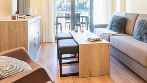 Un salon moderne avec un plancher en bois, un canapé, une table à manger, un téléviseur posé sur un meuble en bois et un balcon offrant une vue sur les arbres.