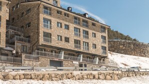 Un immeuble en pierre à plusieurs étages, doté de balcons et d’une façade en pierre, avec un espace de stationnement à l’avant.