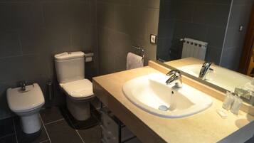 A bathroom with a toilet, bidet, sink, and mirror.