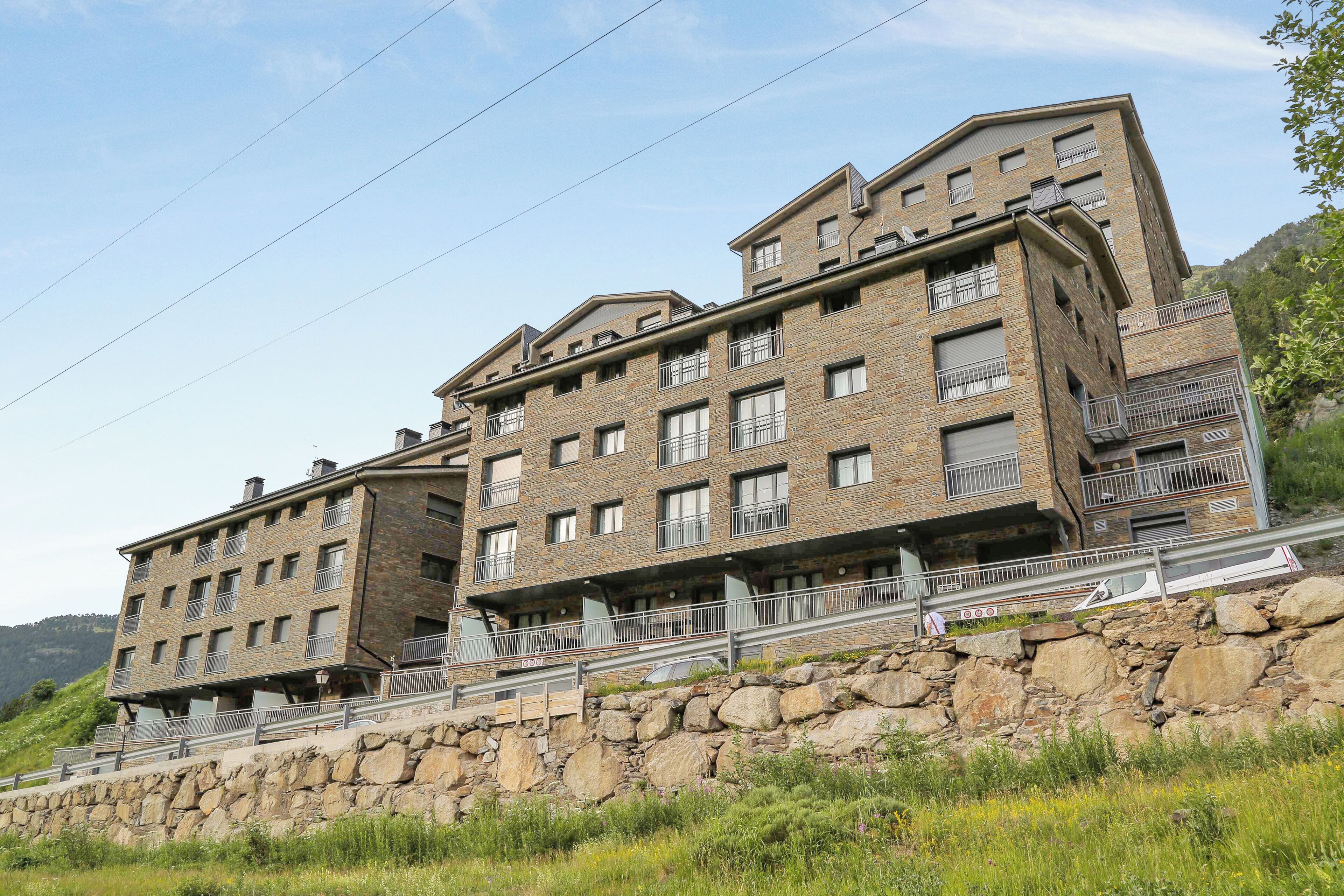 A multi-story hotel with a stone facade, balconies, and a view of the surrounding landscape.