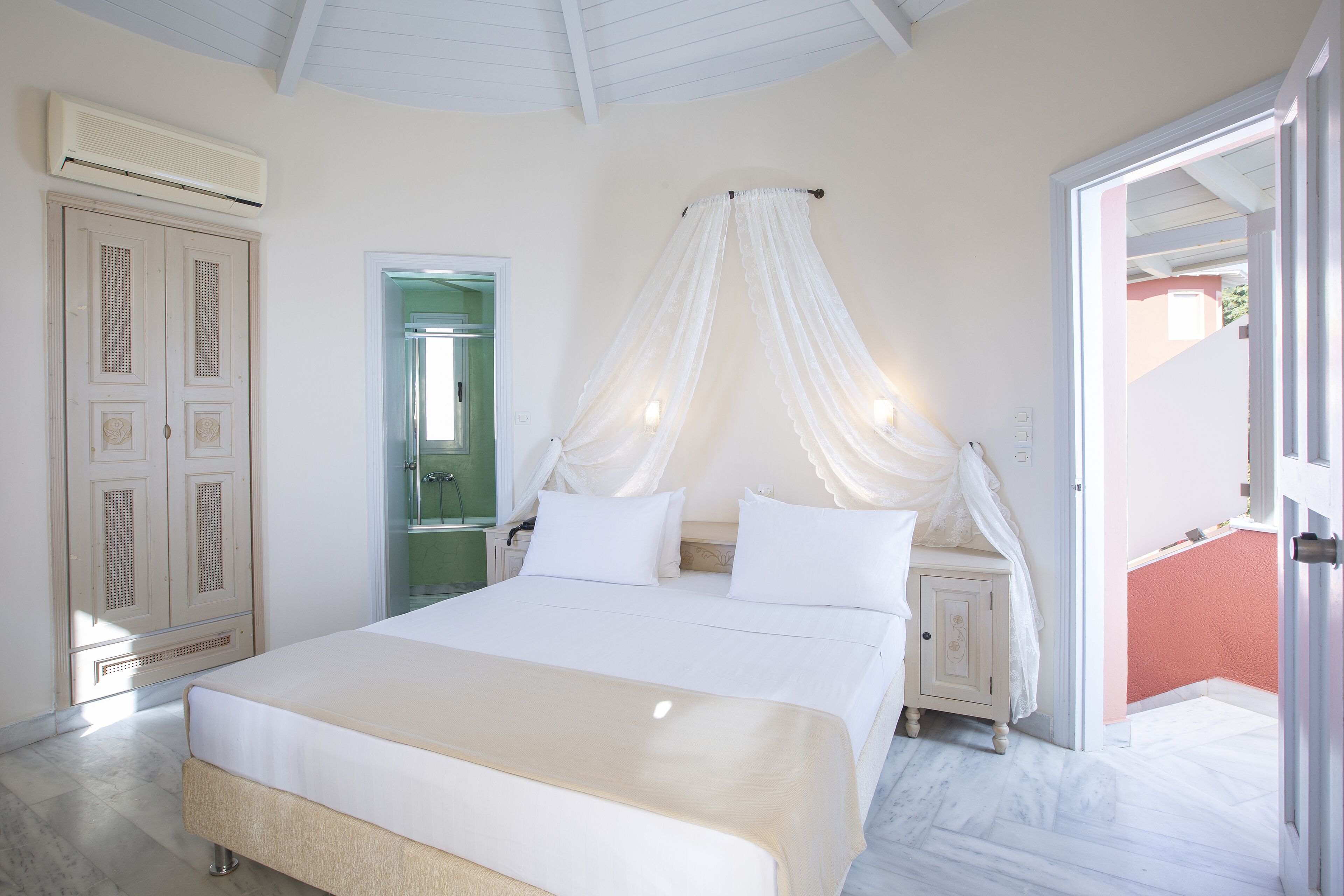 A bedroom with a large bed, a nightstand, a wardrobe, and a door leading to an outdoor area.