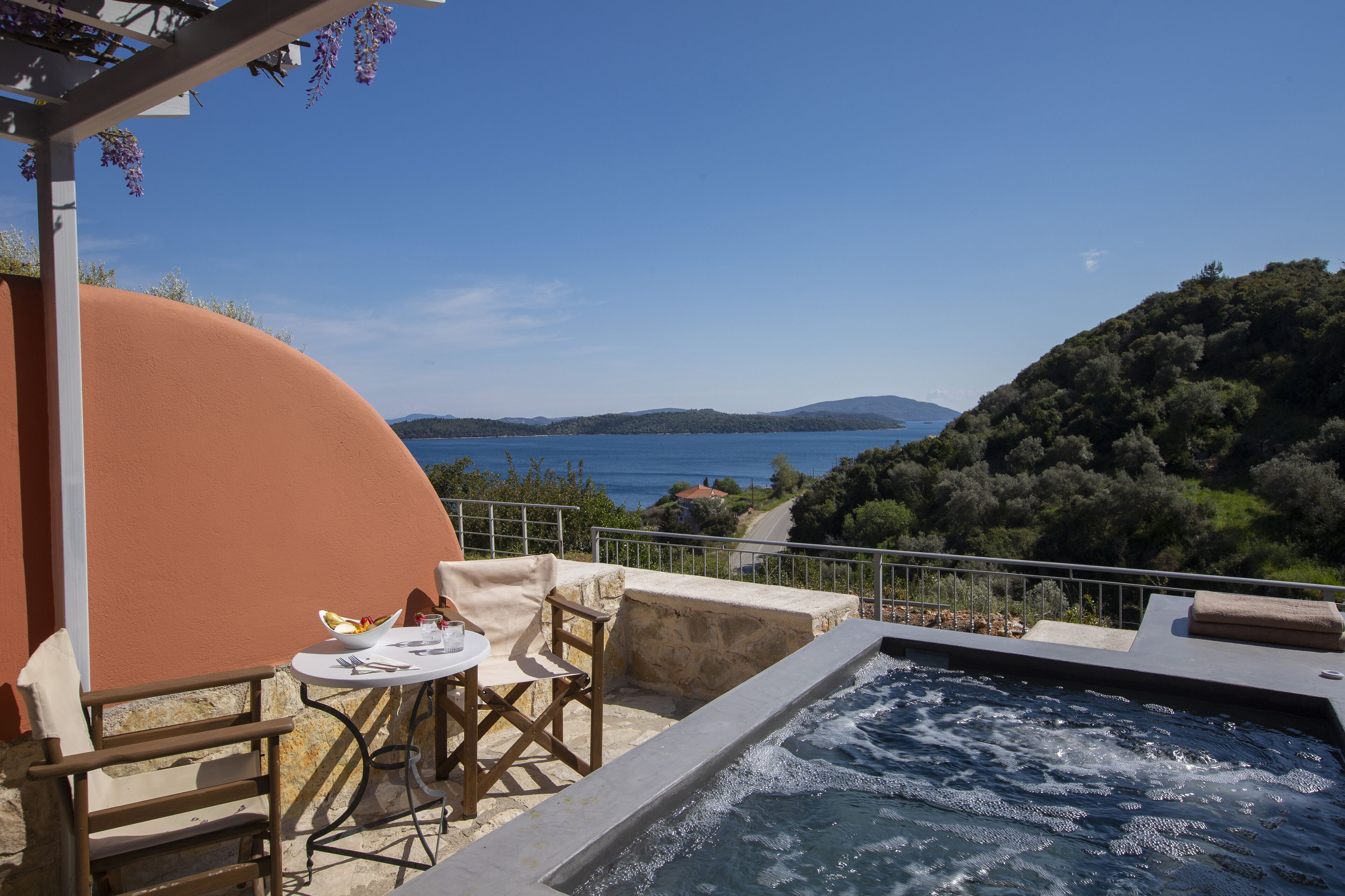 A terrace with a hot tub, outdoor seating, and a view of the sea and hills.