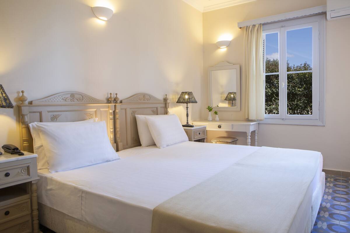 Uma cama bem arrumada com lençóis brancos, uma luminária de cabeceira e uma mesa de cabeceira com um telefone.