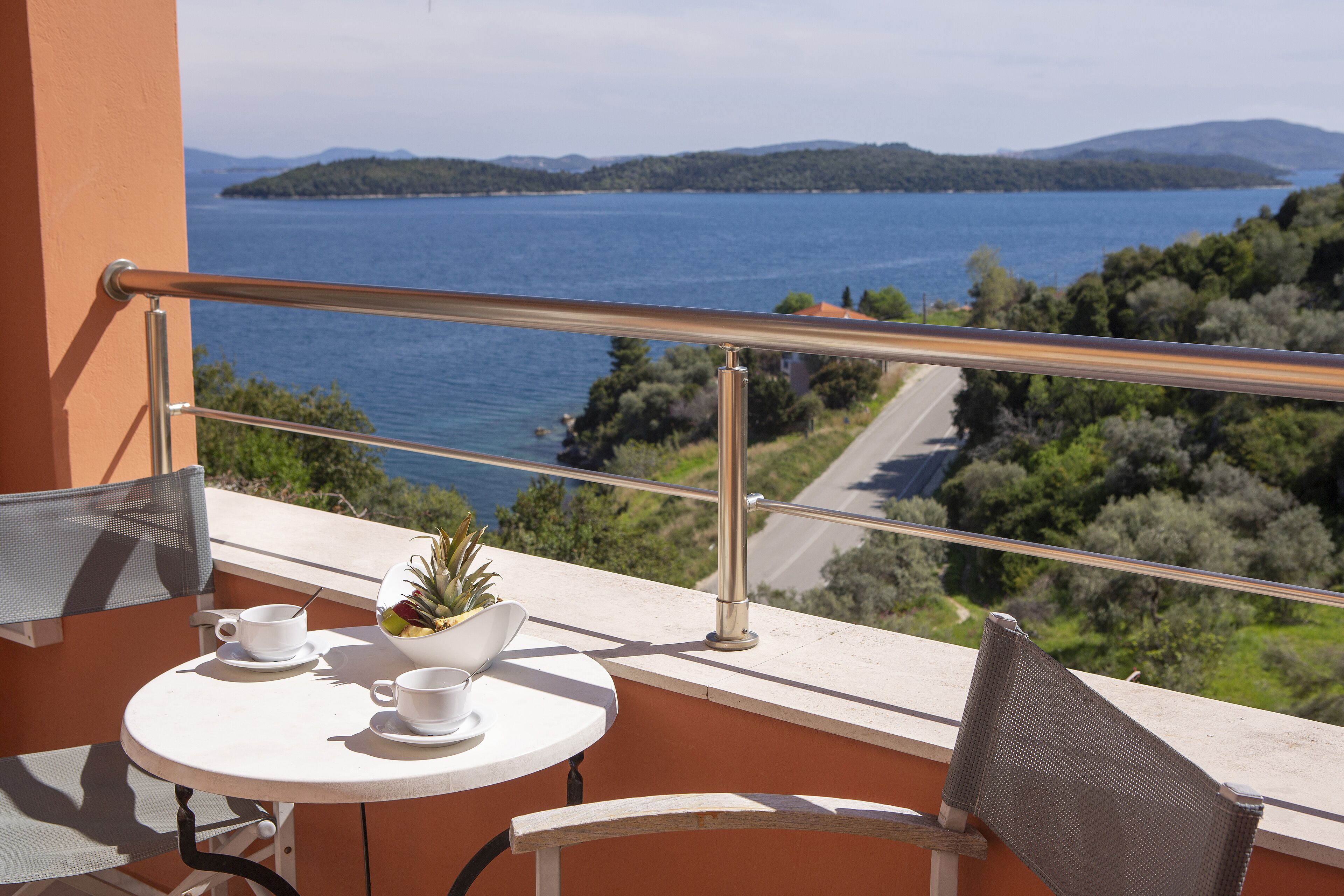A balcony with a table, two chairs, a potted plant, and a view of a lake and mountains.