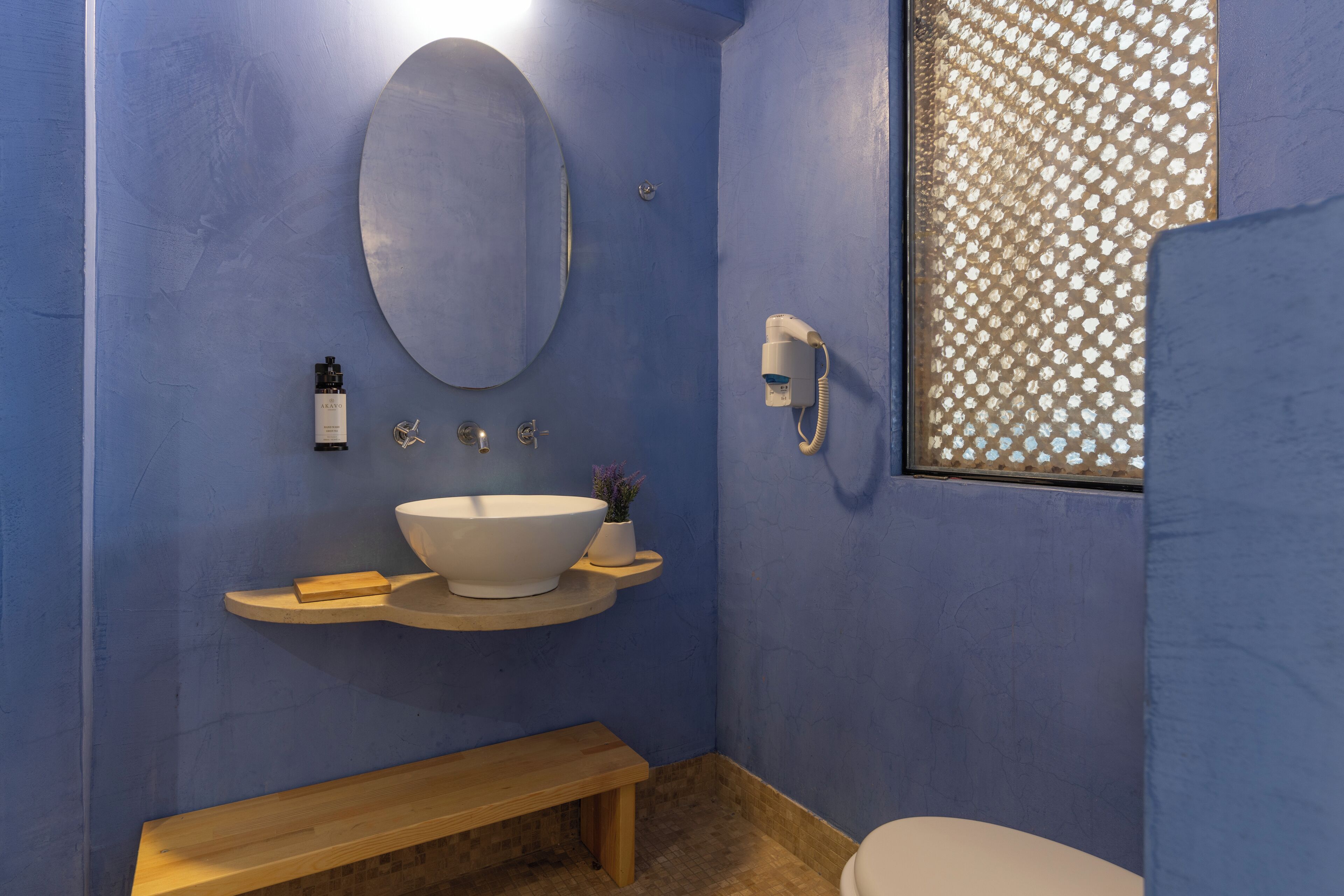 A bathroom with a large oval mirror, a white sink, a handheld showerhead, and a toilet.