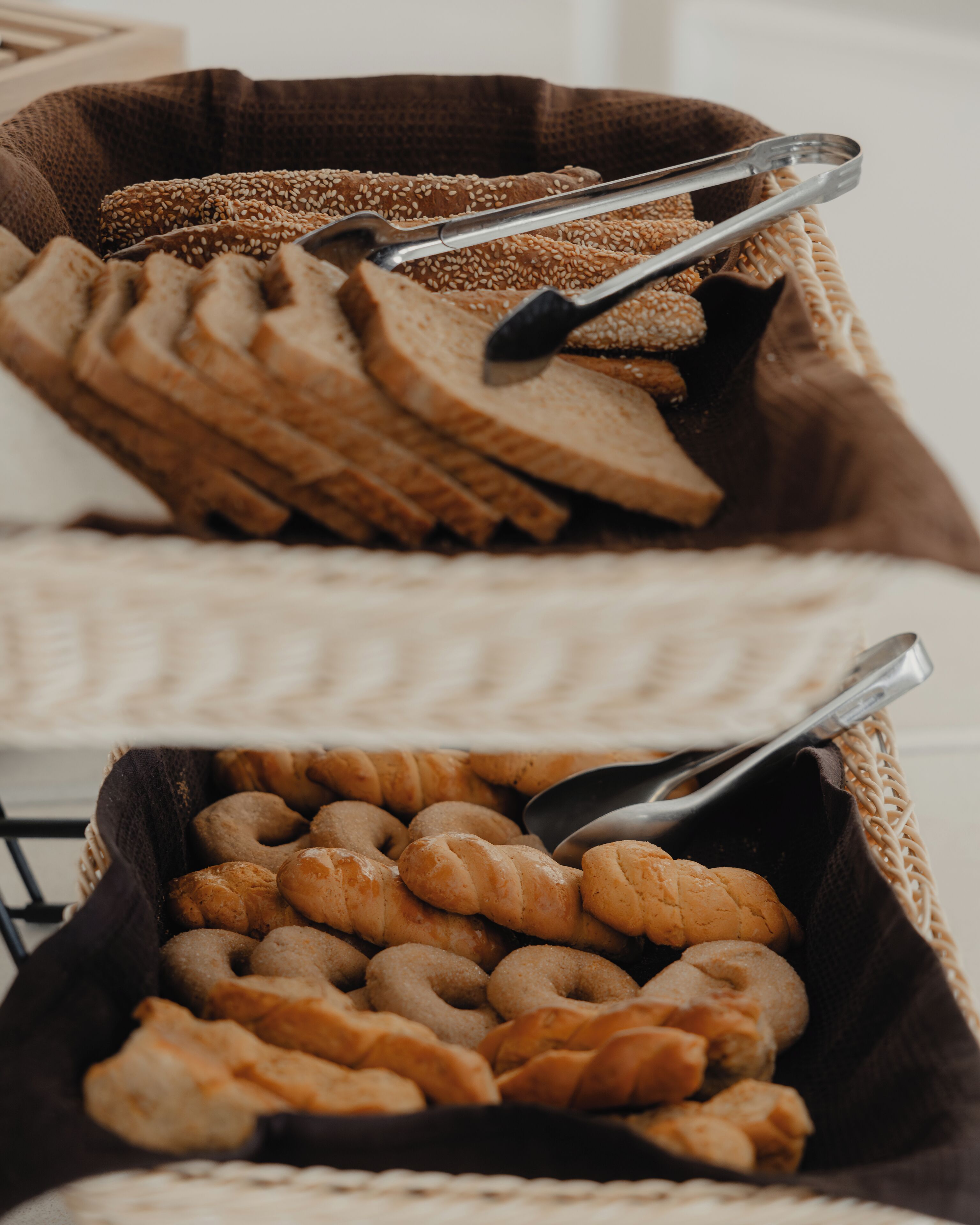 En kurv fyldt med forskellige bagværk, herunder croissanter og sesamruller, med en tang ovenpå.