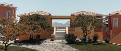 A courtyard with a stone pathway leading to a central staircase, surrounded by buildings with terracotta roofs and orange walls.