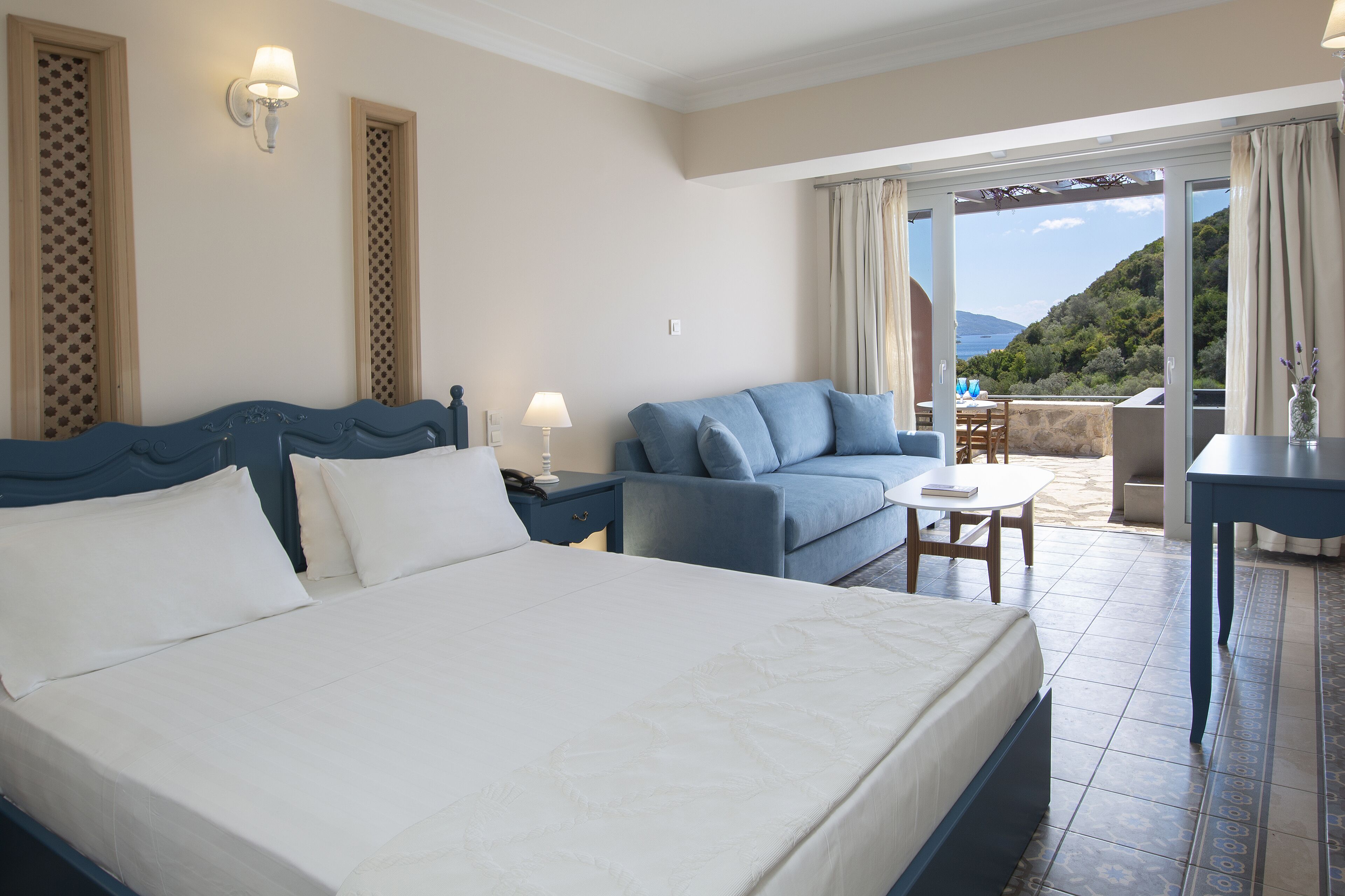 A hotel room with a large bed, a sofa, a small table, and a view of the outdoors.
