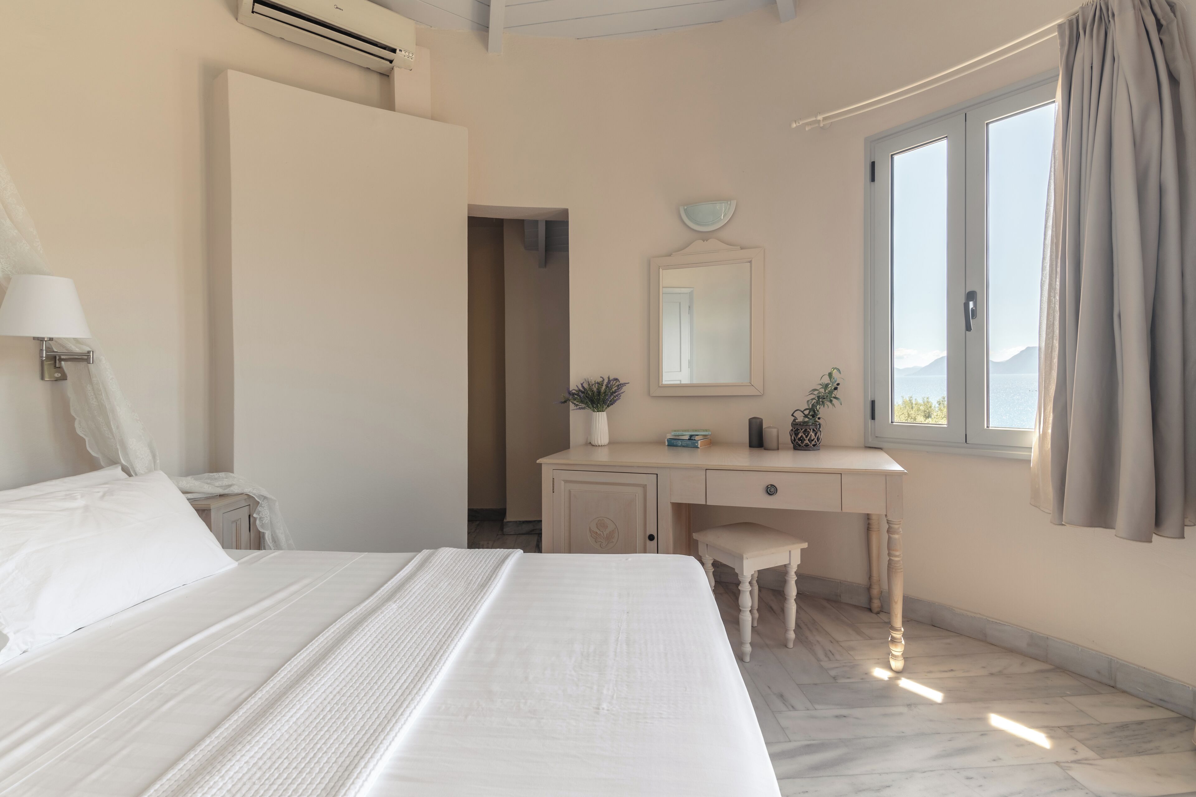 A bedroom with a bed, a desk, a chair, a mirror, and a window with curtains.