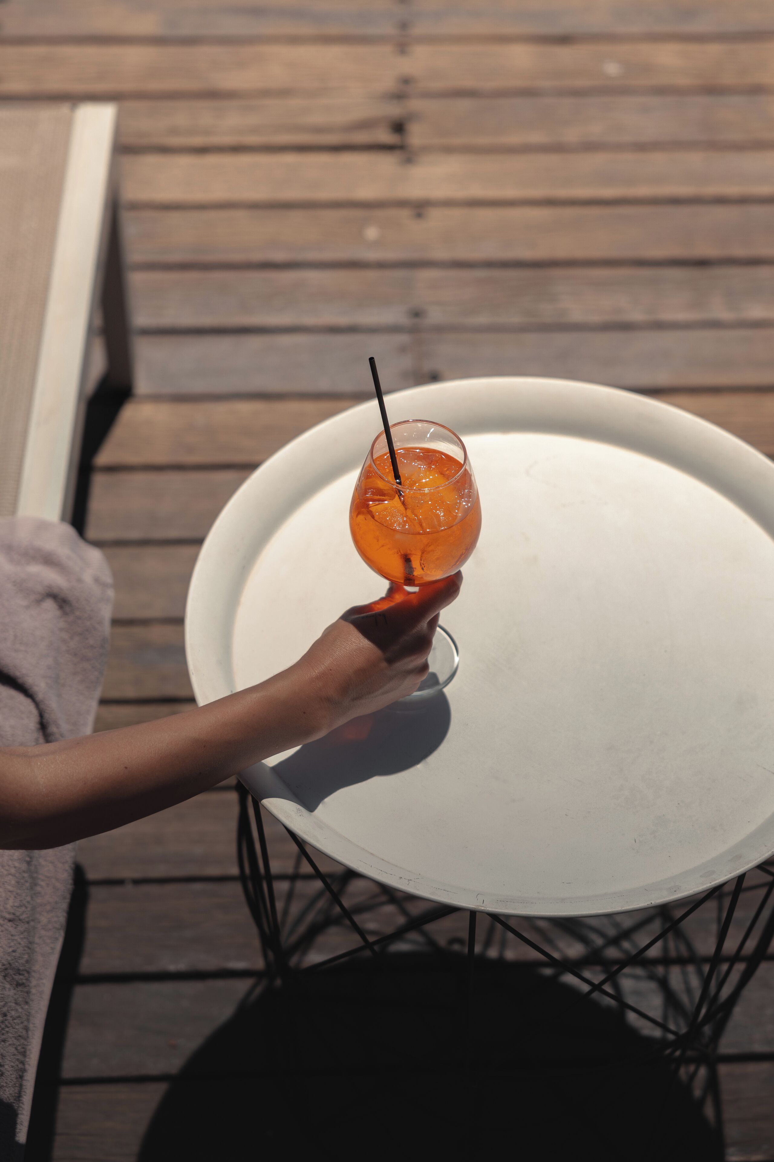A hand holding a glass with an orange drink on a white table outdoors.