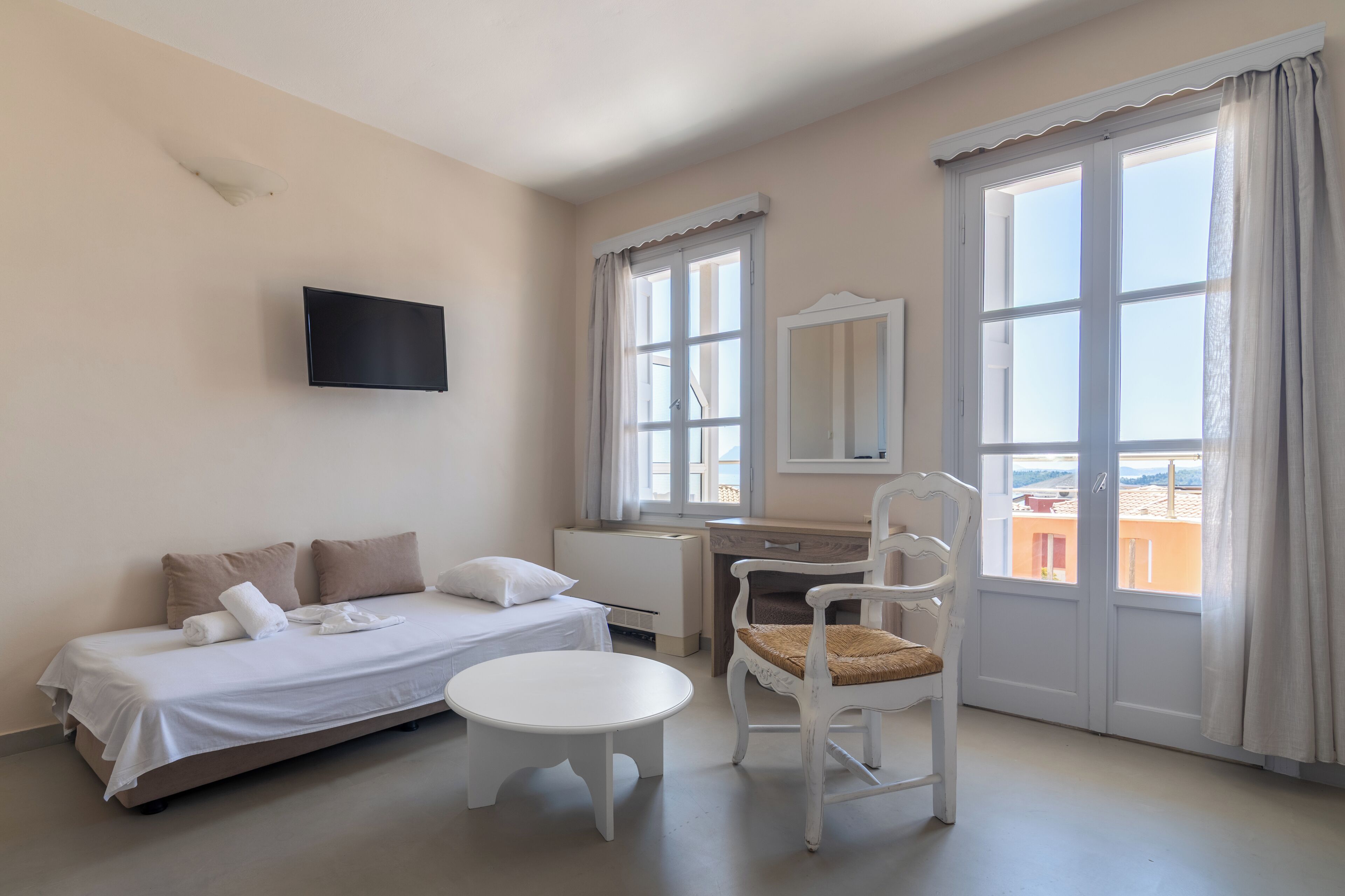 A hotel room with a bed, a desk, a chair, a TV, and large windows.