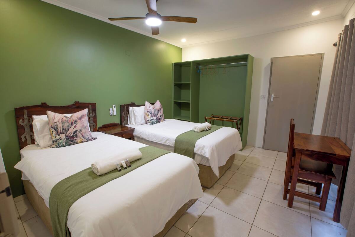 A hotel room with two beds, a wooden chair, a closet, and a ceiling fan.