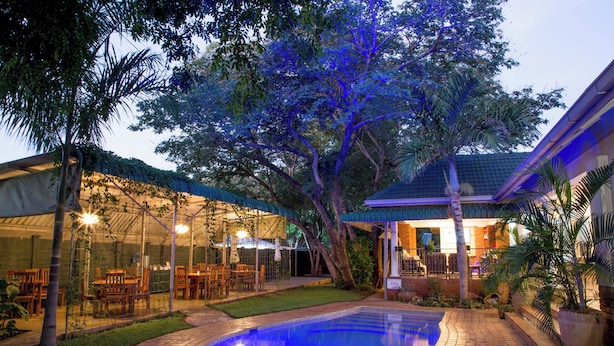 A pool with a tiled edge, surrounded by a brick patio, and a covered outdoor dining area with chairs and tables.