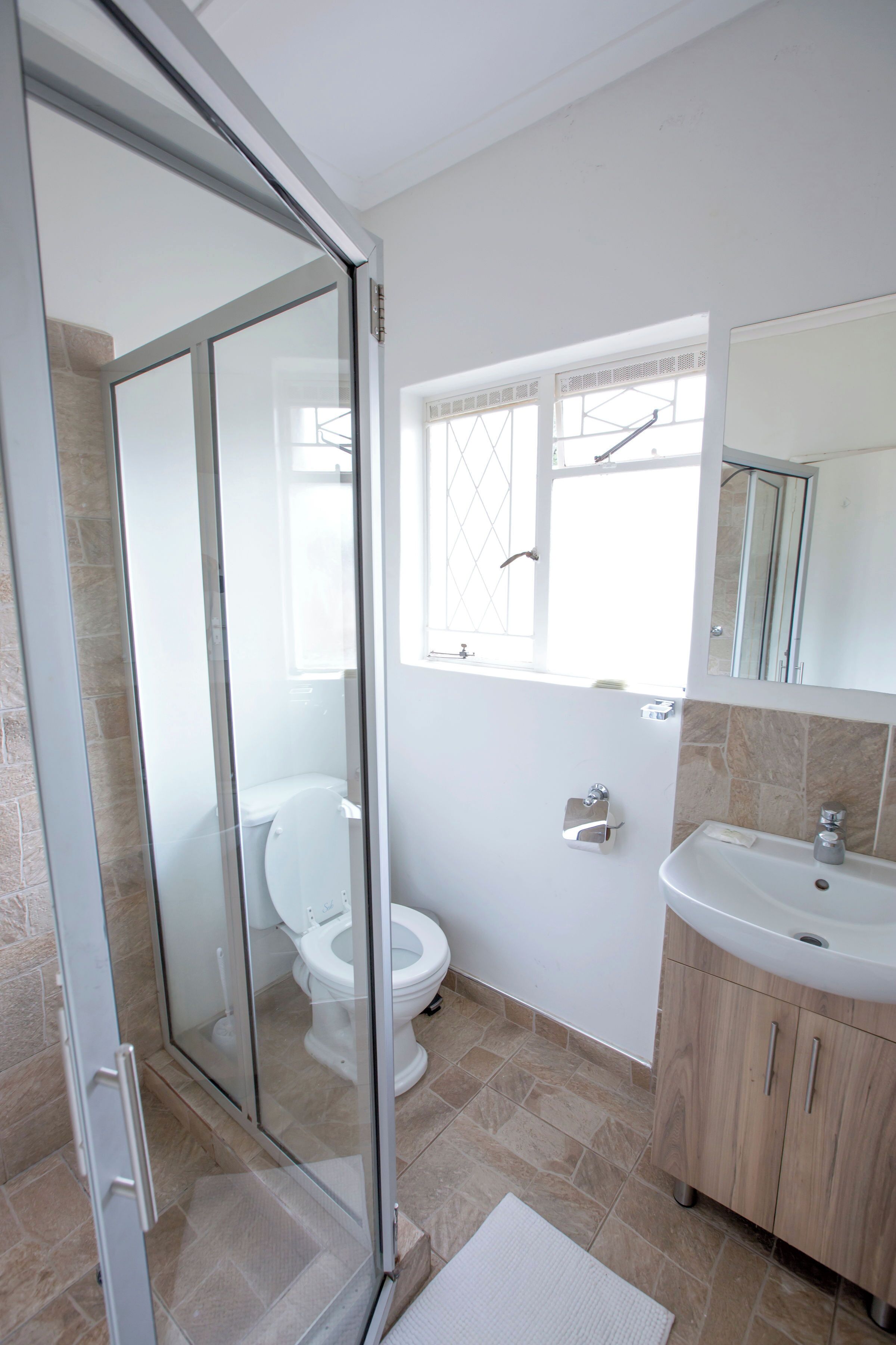 A modern bathroom with a glass shower enclosure, a toilet, a sink, and a window providing natural light.