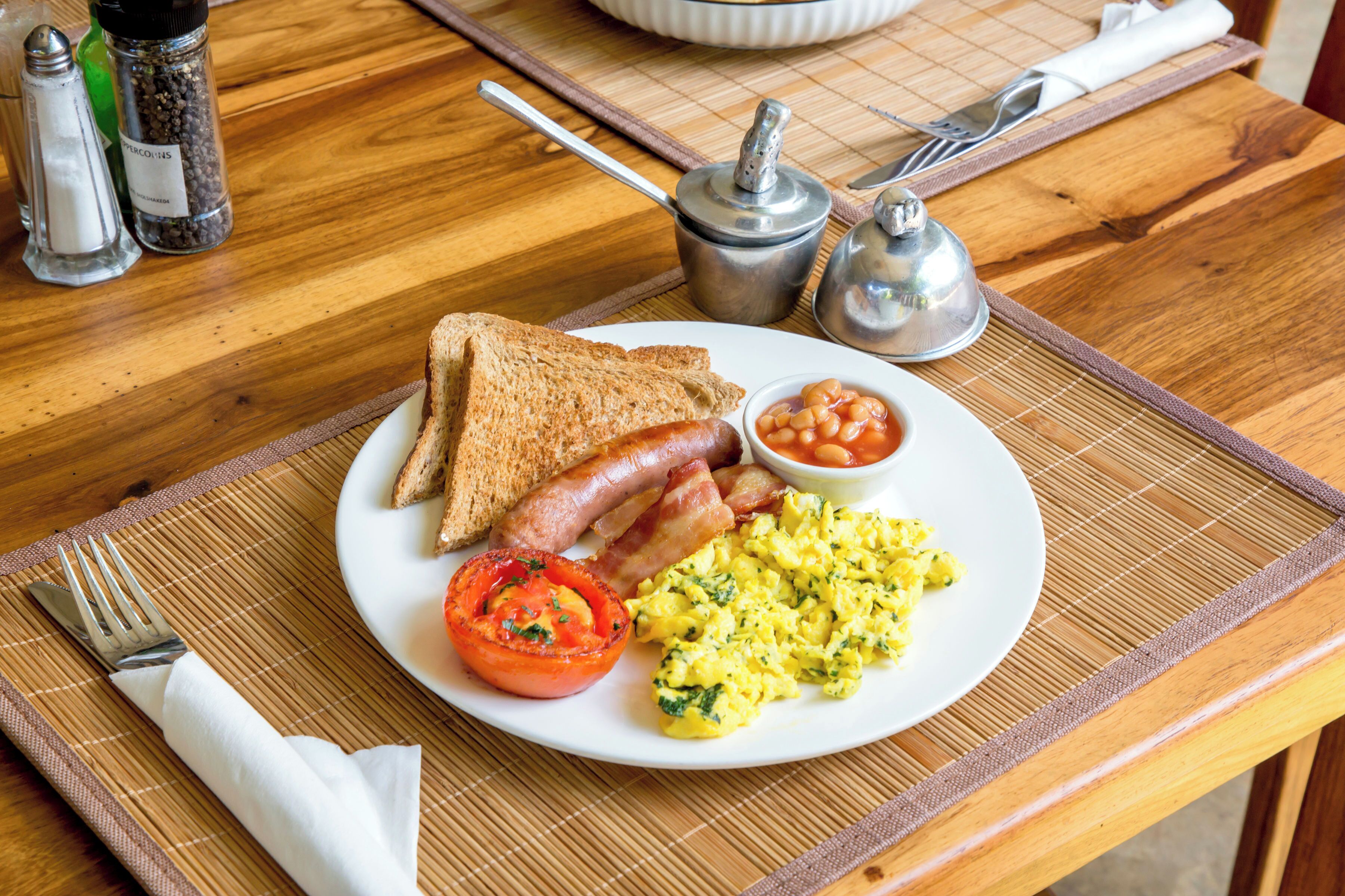 A breakfast plate with toast, bacon, eggs, and beans on a wooden table.