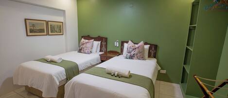 Habitación de hotel con dos camas, ventilador de techo y una pared decorada en color verde.