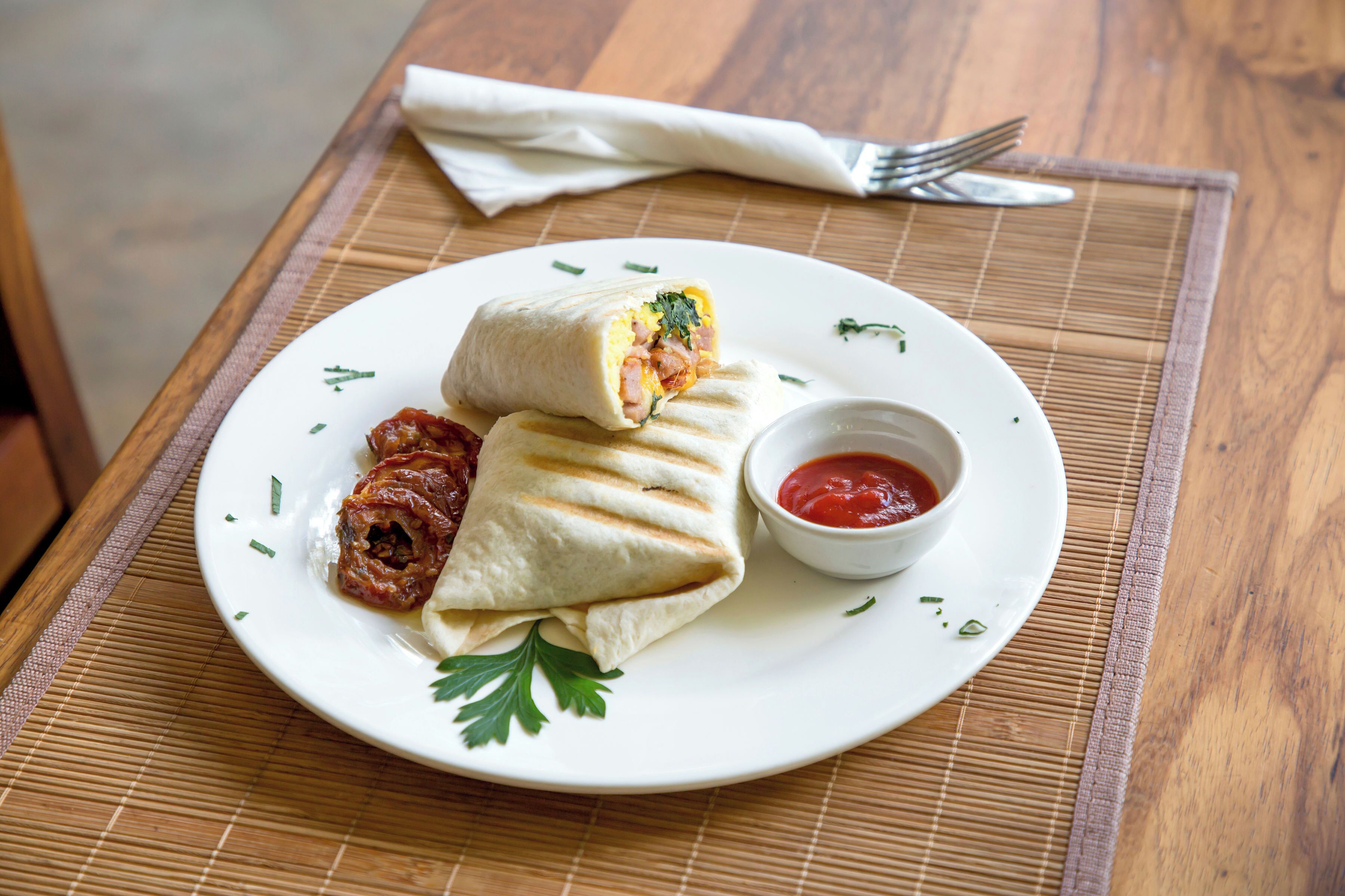 A plate with a wrap, a small bowl of sauce, and a piece of meat on a white plate.