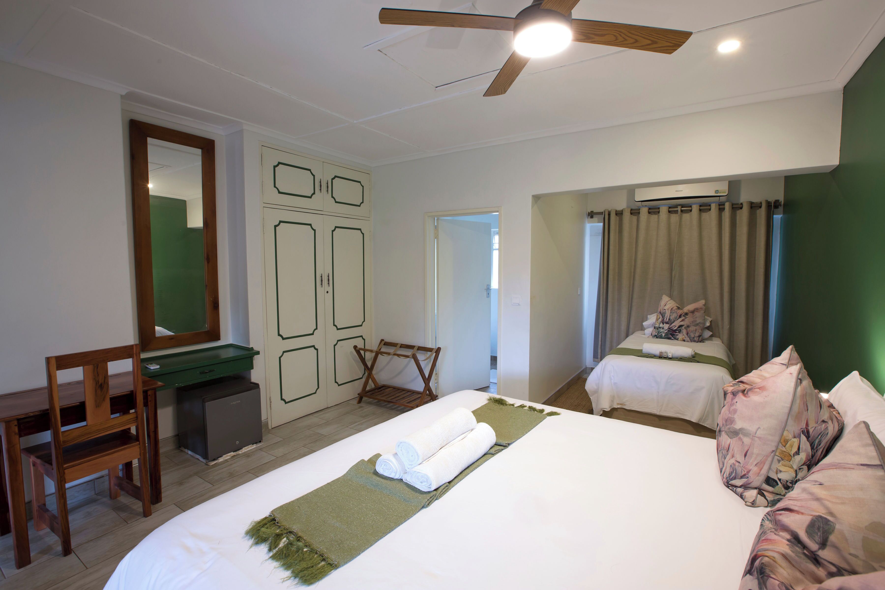 Habitación de hotel con cama, escritorio, silla, armario y ventilador de techo.