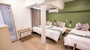 A hotel room with two beds, a wooden bench, a small table, and a green accent wall.