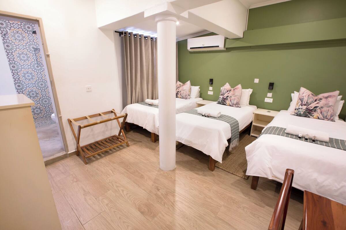 A hotel room with two beds, a wooden bench, a small table, and a green accent wall.