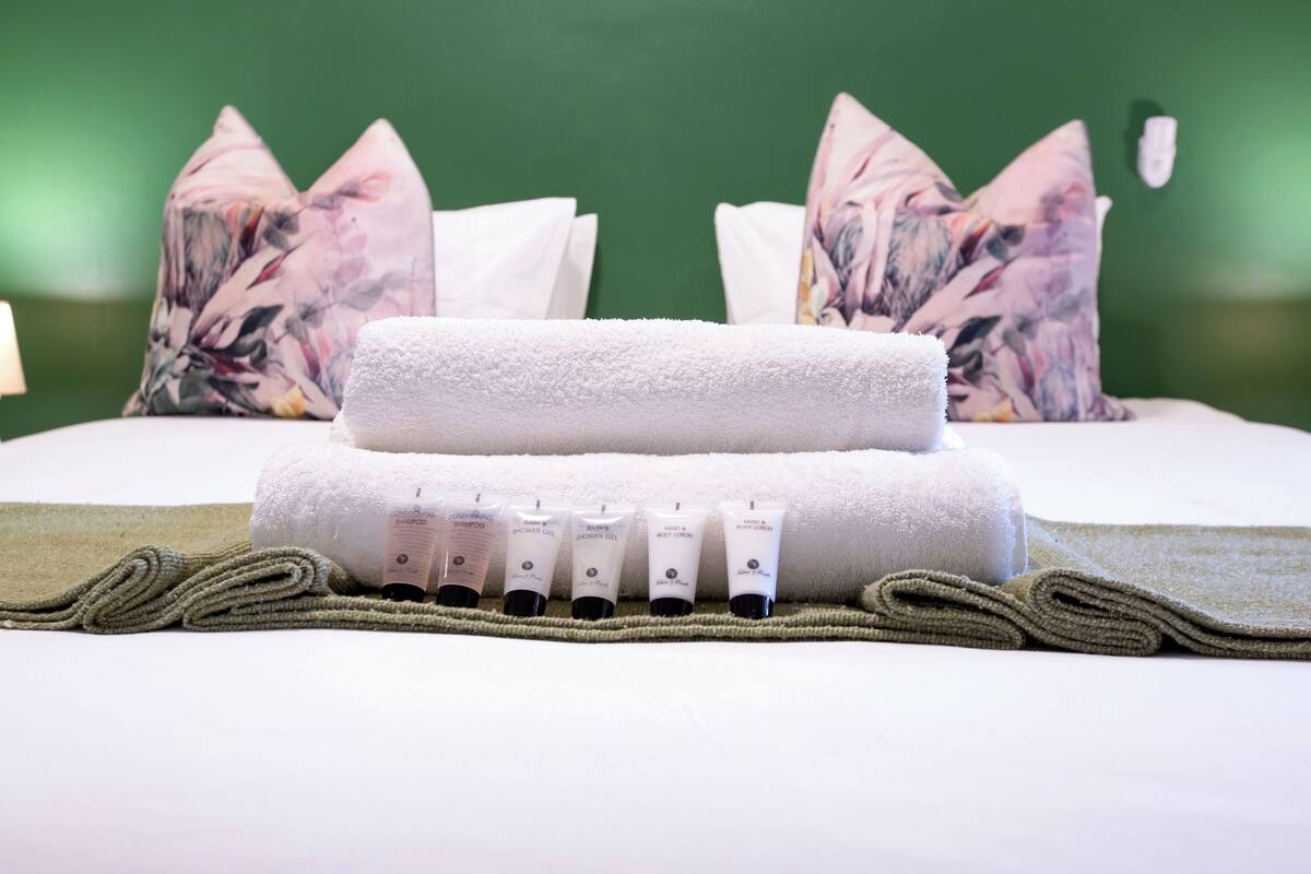 A neatly arranged bathroom with a white towel, a green towel, and five bottles of toiletries on a beige towel.