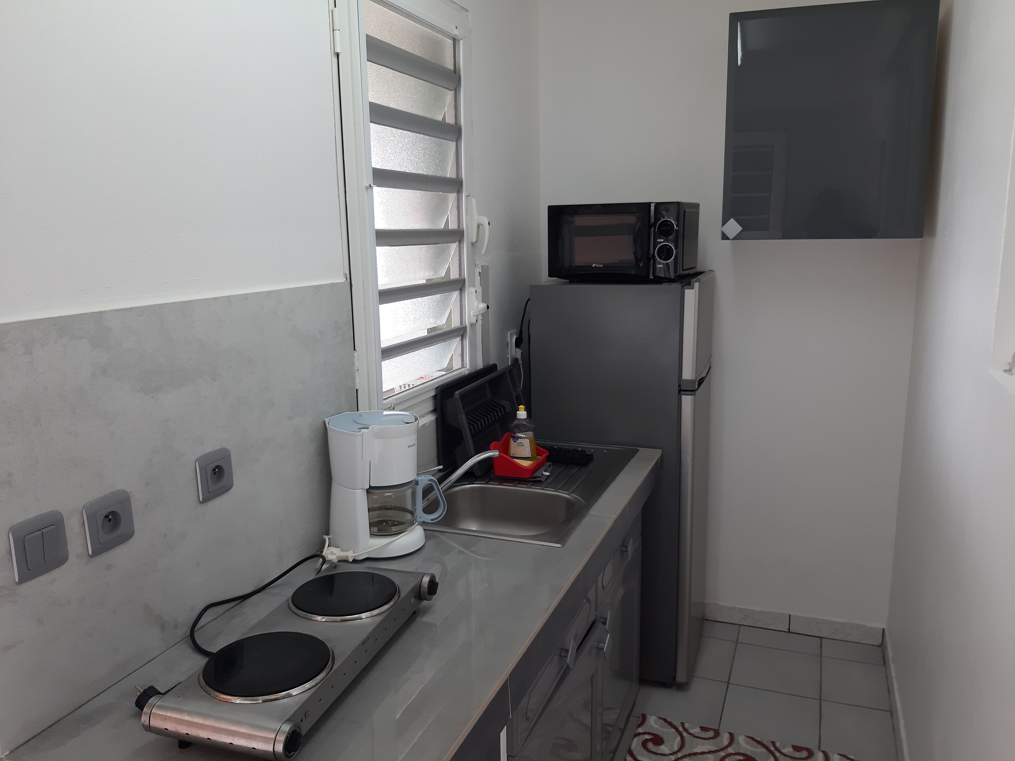 Una kitchenette compacta con microondas, cafetera y refrigerador pequeño.
