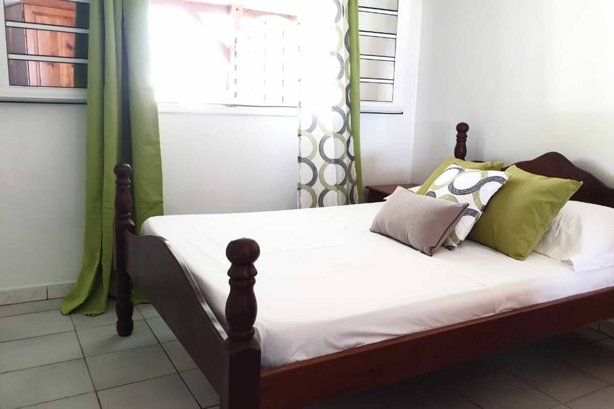 Una cama bien hecha con estructura de madera y ropa de cama blanca, complementada con varios almohadones de distintos colores.