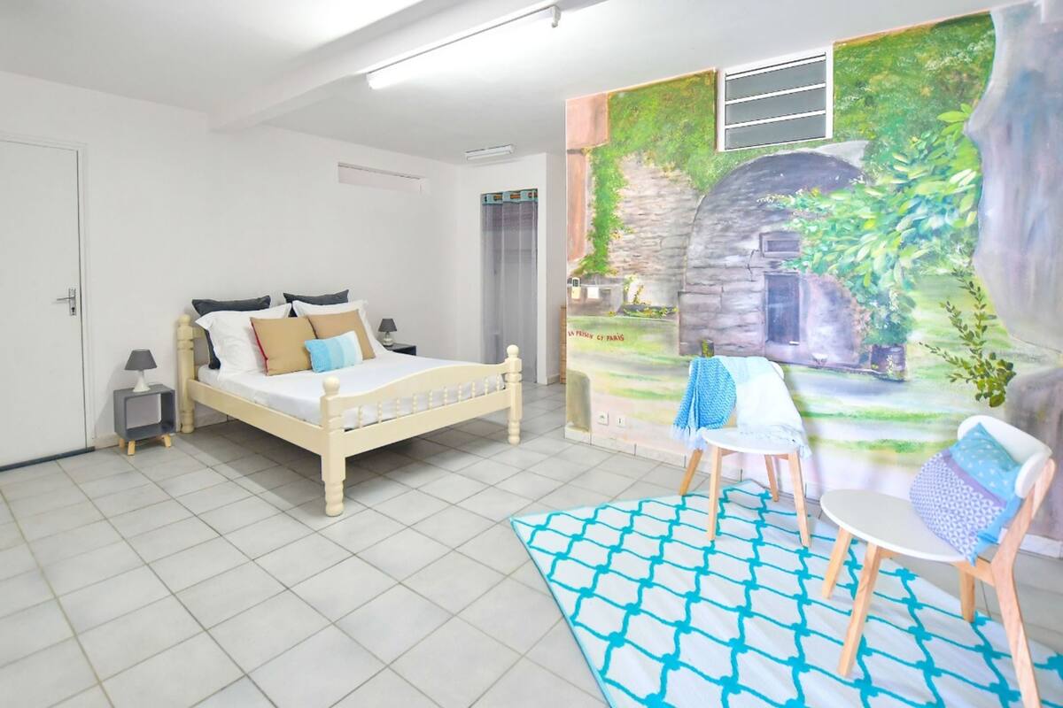 Un dormitorio con cama, una silla, una mesita y un mural en la pared.