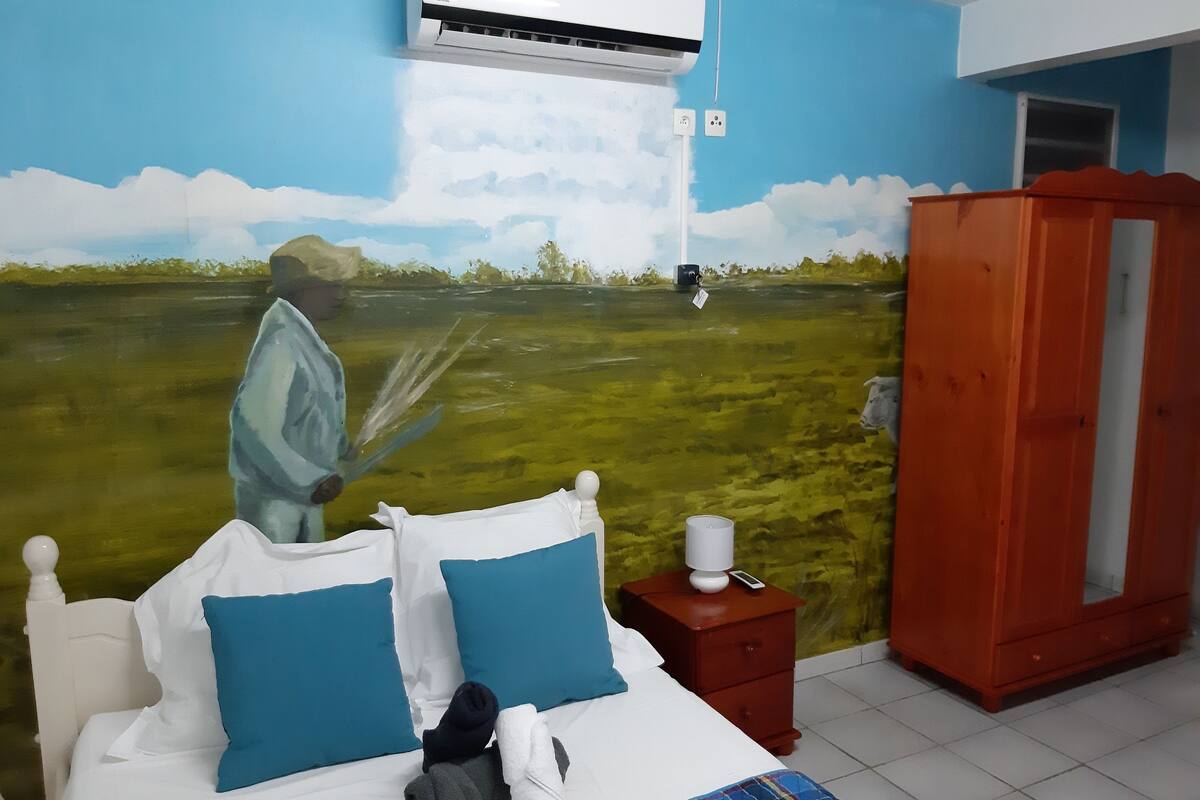 Habitación de hotel con cama, mesita de noche, armario y un mural de un paisaje.