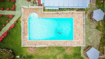 Vista aérea de una piscina rectangular rodeada de muros de piedra y césped verde.