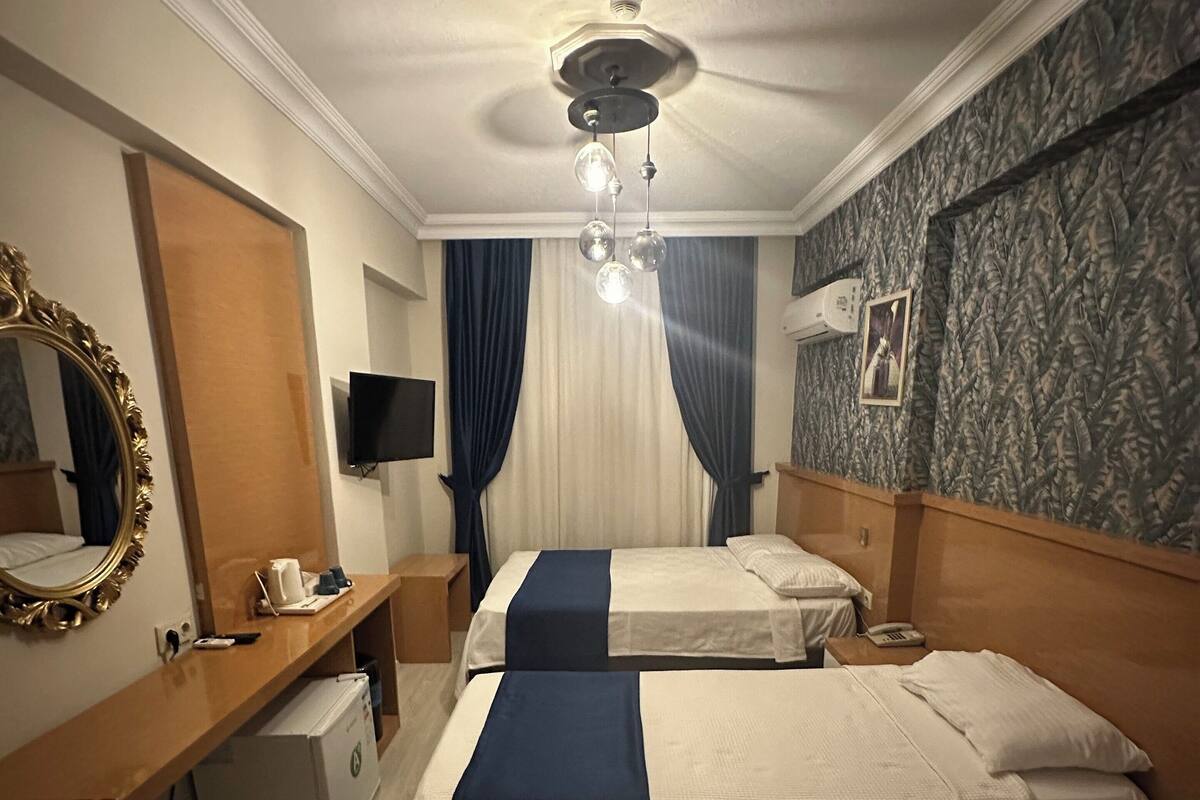 Een hotelkamer met twee bedden, een bureau met telefoon, een spiegel en een plafondventilator.
