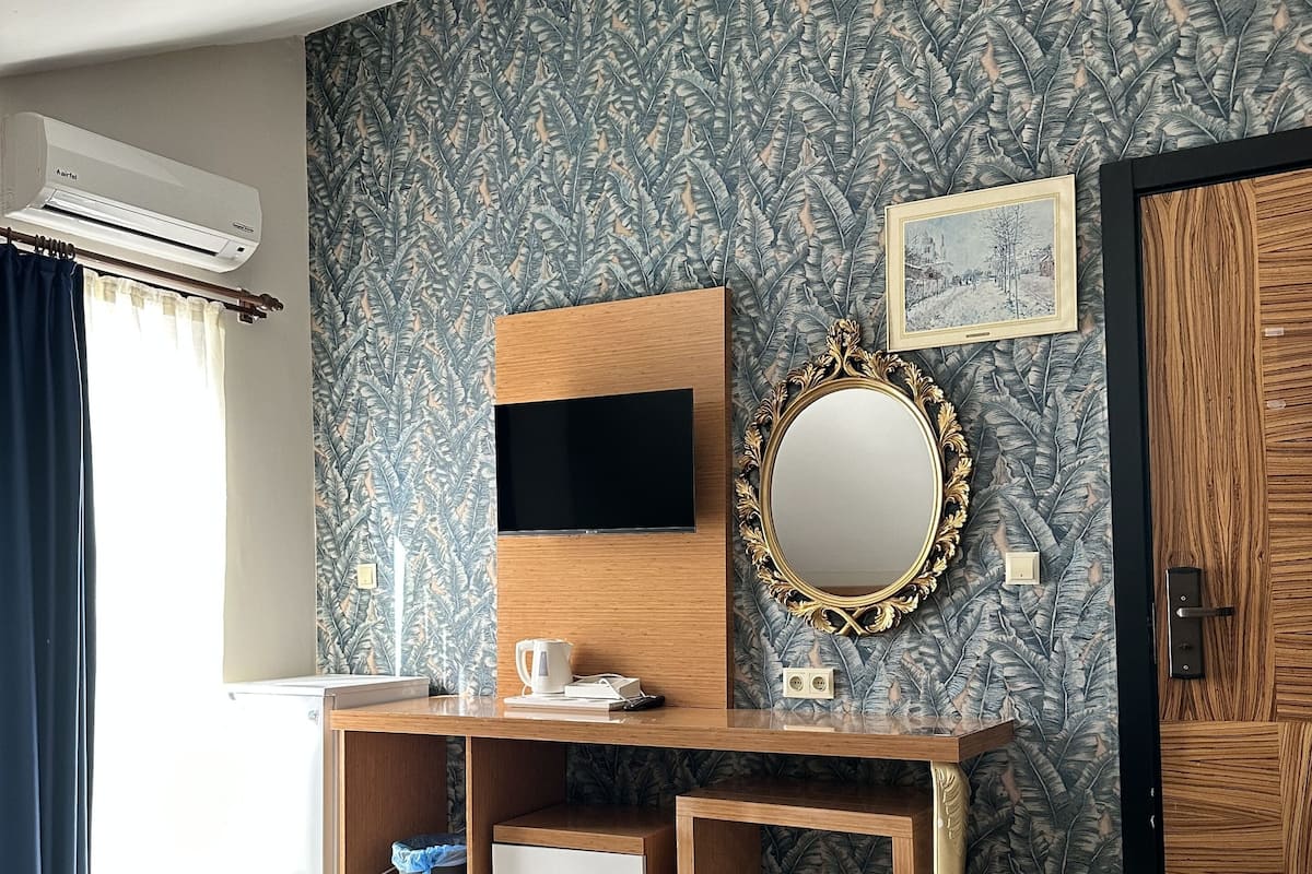Een hotelkamer met twee bedden, een houten bureau met een televisie, een spiegel en een schilderij aan de muur.