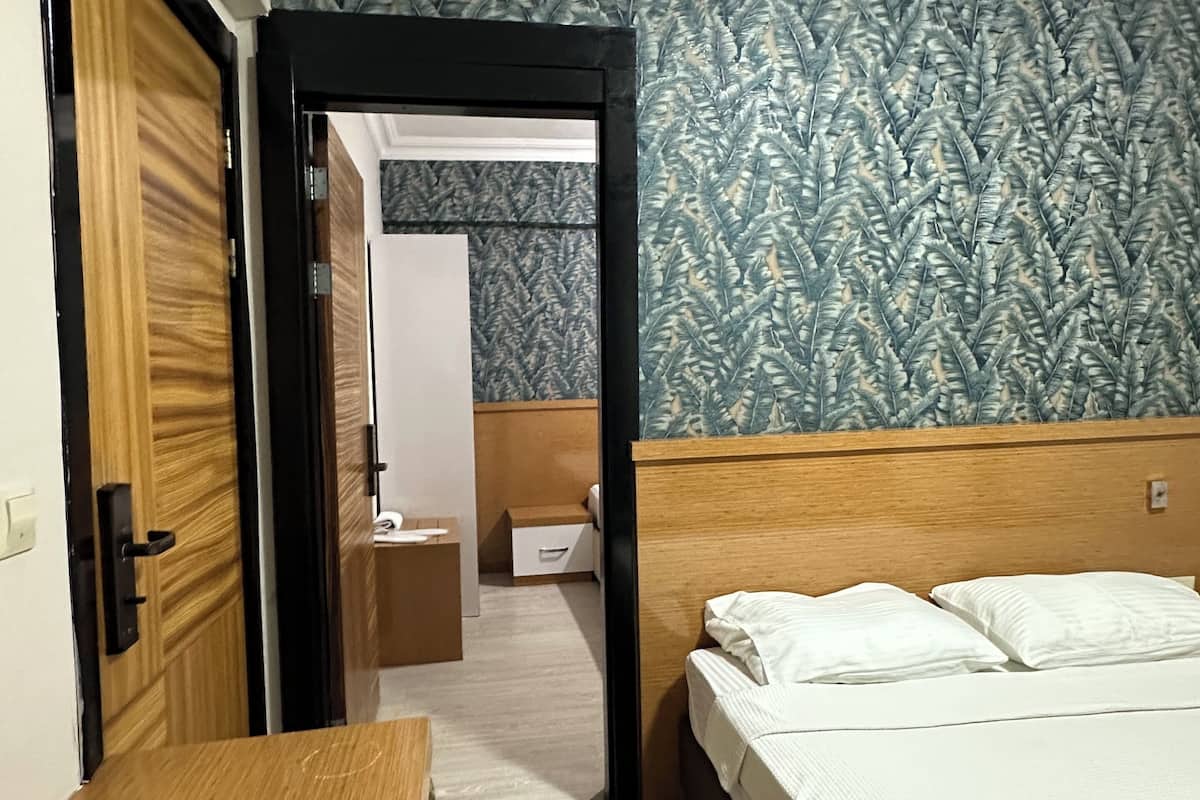 Een hotelkamer met een bed, een houten bureau, een kledingkast en een badkamer die door een open deur zichtbaar is.