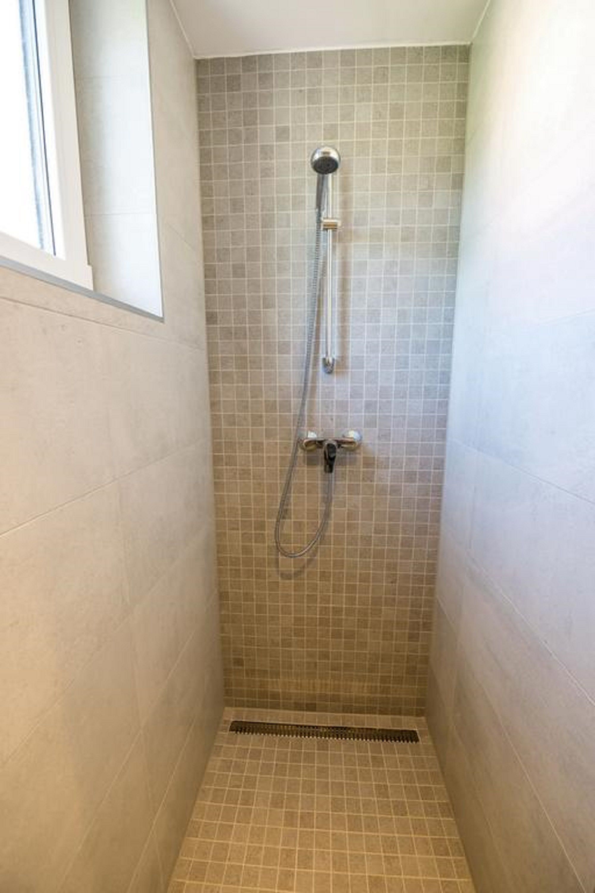 A small, tiled shower room with a single showerhead and a drain.
