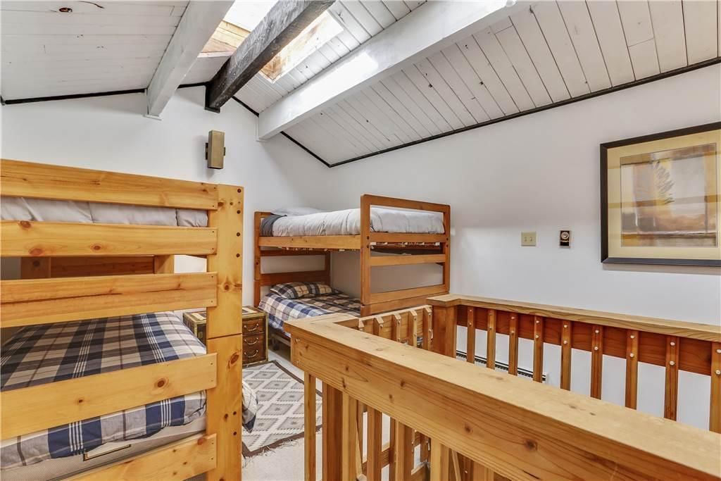 Habitación tipo dormitorio con literas, baranda de madera, tragaluz e imagen en un marco en la pared.