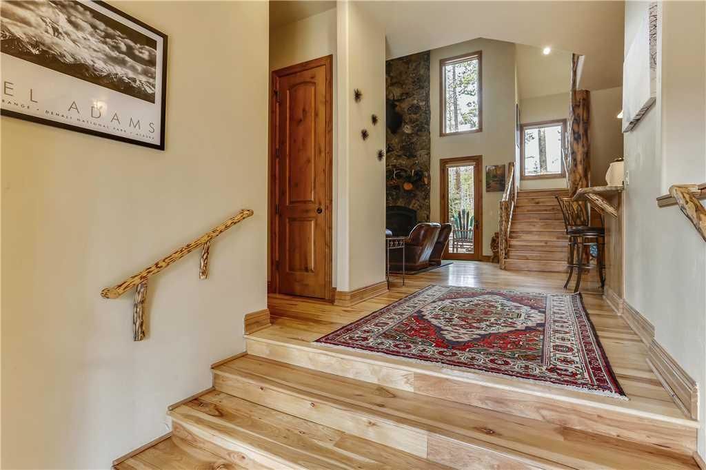 Un escalier en bois, surmonté d’un tapis rouge à motifs, mène à un coin repas agrémenté d’un mur en pierre et offrant une vue sur l’extérieur.