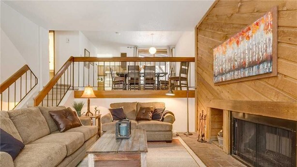 A cozy living room with a fireplace, a staircase leading to an upper level, and a dining area in the background. - Winter Point 17 Town House (Breckenridge)