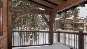 A wooden balcony with a metal railing overlooking a snowy landscape with trees and buildings. - Winter Point 17 Town House (Breckenridge)