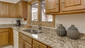A kitchen with wooden cabinets, granite countertops, a stainless steel sink, and two decorative vases. - Winter Point 17 Town House (Breckenridge)