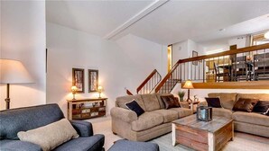 A spacious living room with a large sofa set, a coffee table, and a staircase leading to an upper level. - Winter Point 17 Town House (Breckenridge)