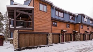 A multi-story wooden building with a stone foundation, featuring large windows and a covered porch. - Winter Point 17 Town House (Breckenridge)