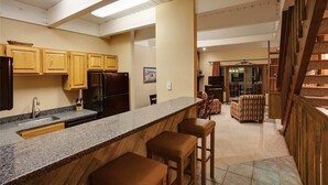 A kitchen with granite countertops, wooden cabinets, and a built-in refrigerator. There are two bar stools and a dining area with a patterned rug. - Winterwood 3 Town House (Steamboat Springs)