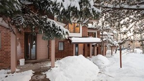 A brick building with a covered porch and snow-covered trees. - Winterwood 3 Town House (Steamboat Springs)