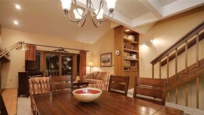 A dining area with a wooden table and chairs, a chandelier, and a staircase with wooden railings. - Winterwood 3 Town House (Steamboat Springs)