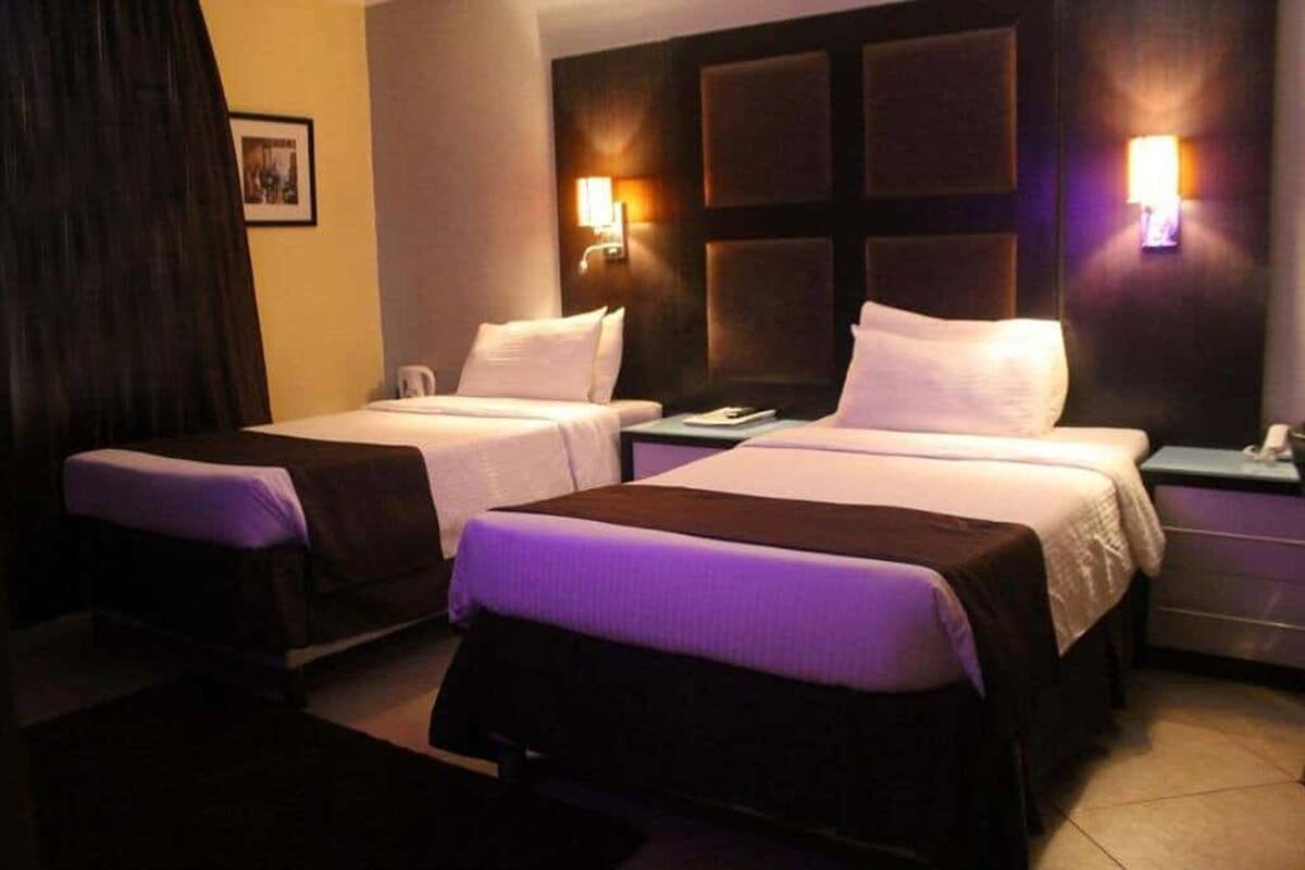 A hotel room with two beds, a nightstand, and wall-mounted lamps.