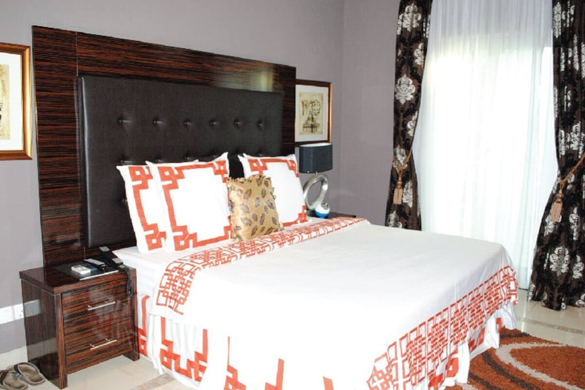 A bedroom with a large bed, a wooden nightstand, a bedside table, a lamp, and a framed picture on the wall.