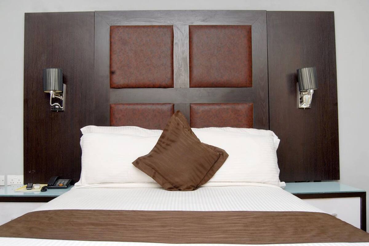 A hotel room with a large bed, a wooden headboard, two bedside lamps, and a nightstand with a phone.