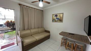 A living room with a sofa, a ceiling fan, a painting, a TV, and a small table with stools.