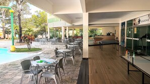 Een terras buiten met tafels en stoelen, een zwembad en een tafeltennistafel.
